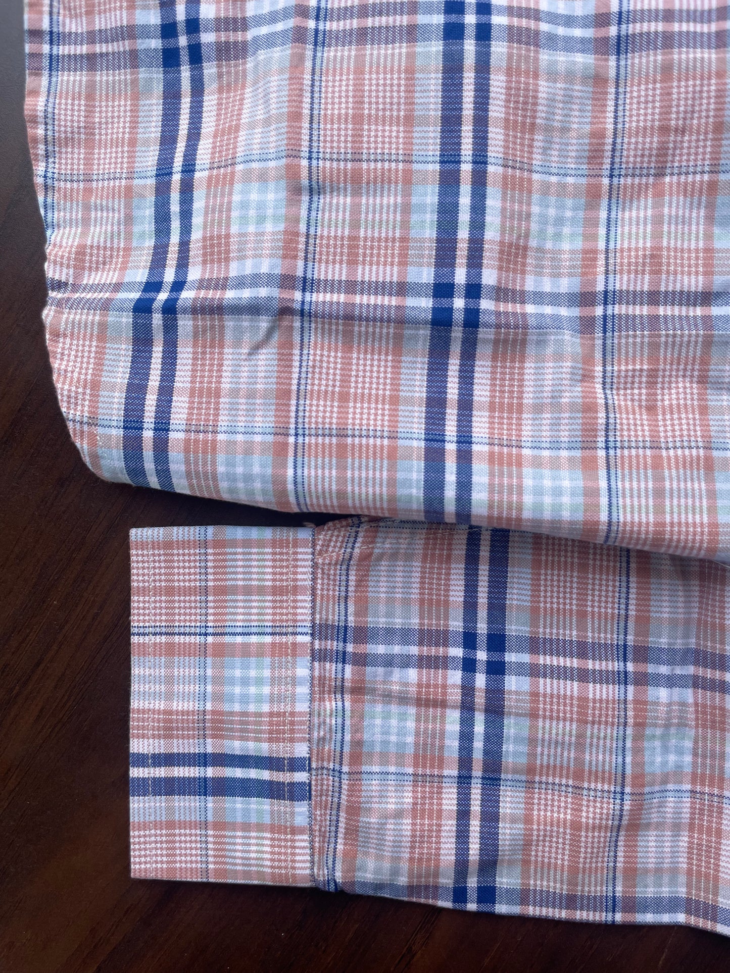 Pink and blue plaid cotton shirt hem and folded sleeve, buttoned panel visible