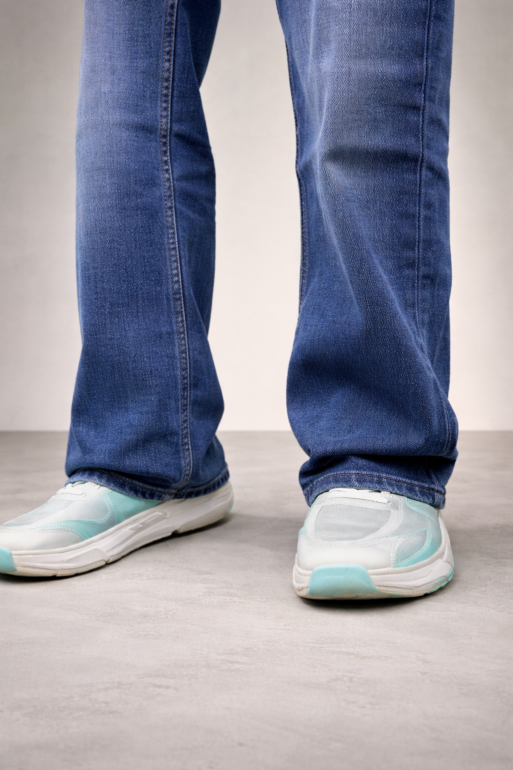 Indigo straight-fit jeans showing rolled cuffs and hem stitching near sneakers.