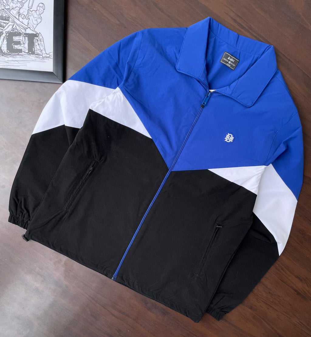 Laid-flat windbreaker jacket in royal blue, white, and black with zip closure and chest logo