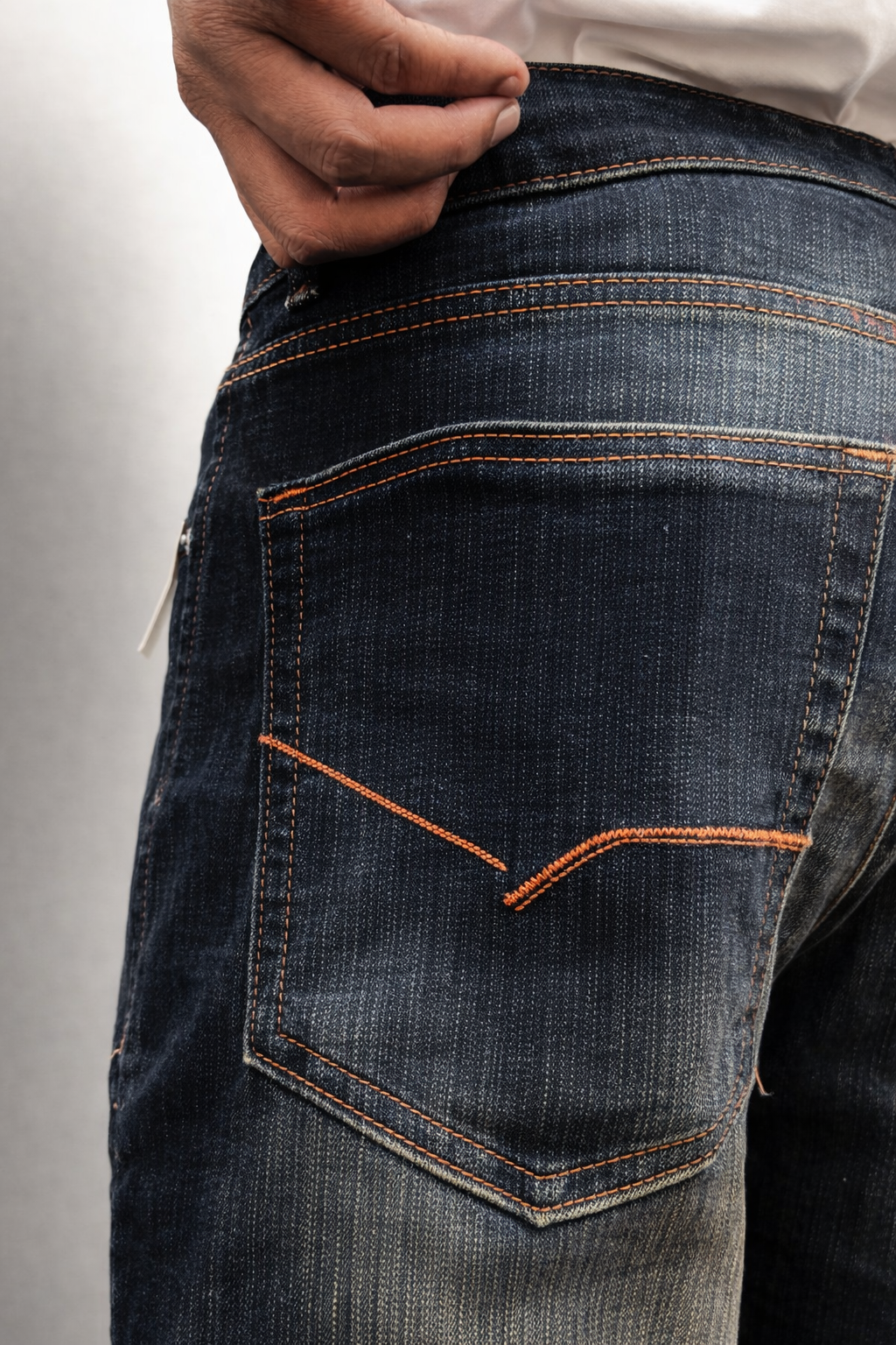 Back pocket close-up showing dark indigo denim texture and orange contrast thread.