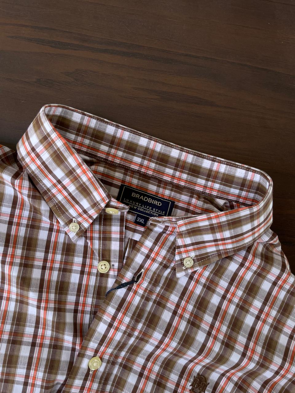 Brown, orange, and white plaid button-up shirt neckline with collar and inner tag