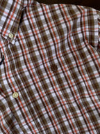 Close-up brown, orange, and white plaid shirt with button placket and chest emblem