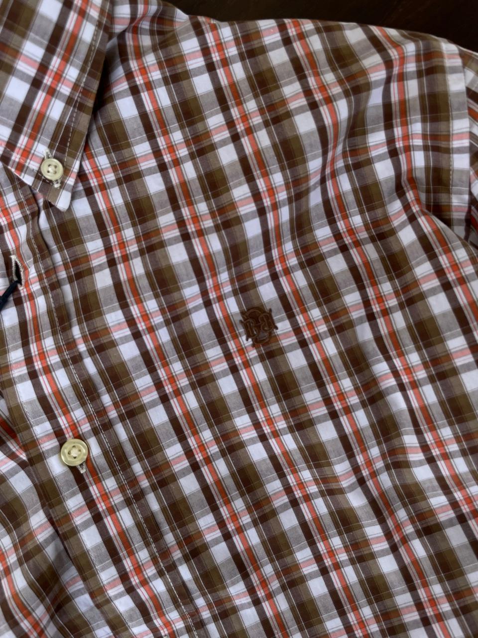 Close-up brown, orange, and white plaid shirt with button placket and chest emblem