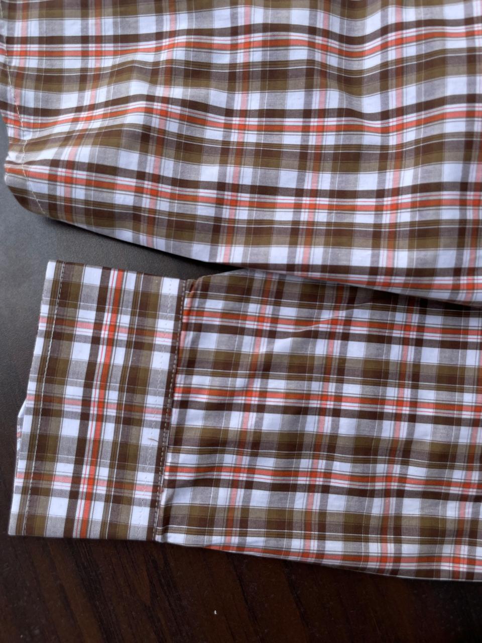 Brown, orange, and white plaid long sleeves with button cuffs, laid flat