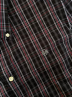 Close-up of dark plaid fabric with red-and-white lines and embroidered chest emblem