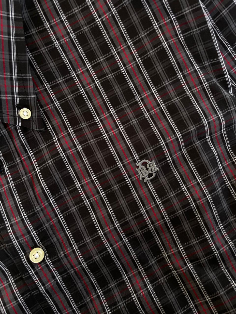 Close-up of dark plaid fabric with red-and-white lines and embroidered chest emblem