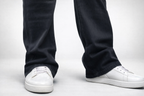 Lower leg view: dark denim jeans hem and white sneakers with lace-up detail