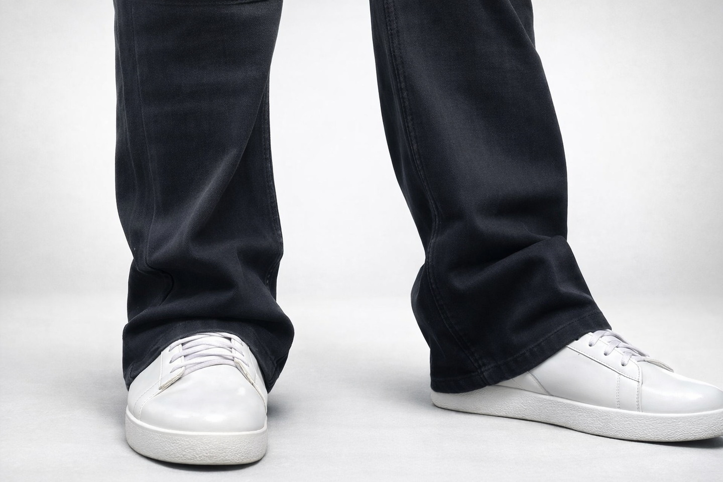 Lower leg view: dark denim jeans hem and white sneakers with lace-up detail