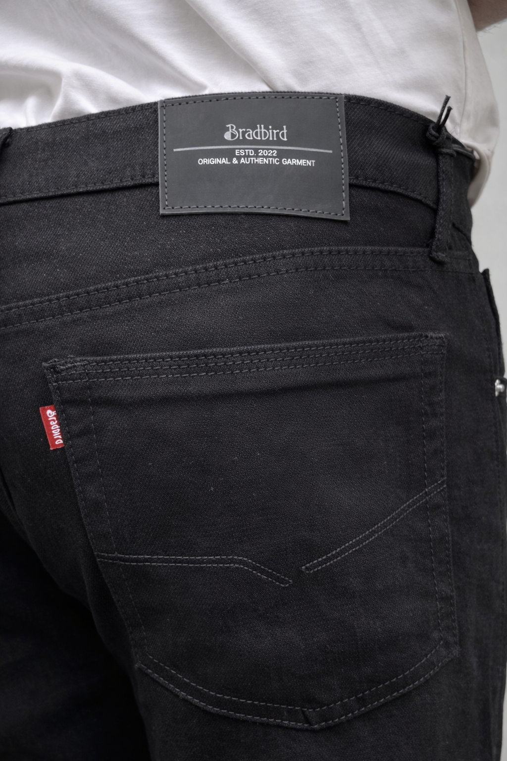 Men's jet black straight-fit jeans, close-up of back pocket and logo patch