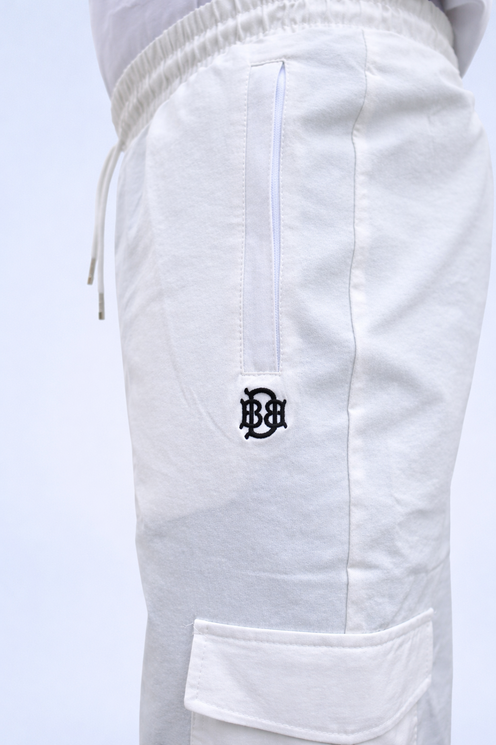White joggers close-up: elastic waist, side pocket with embroidered logo on leg