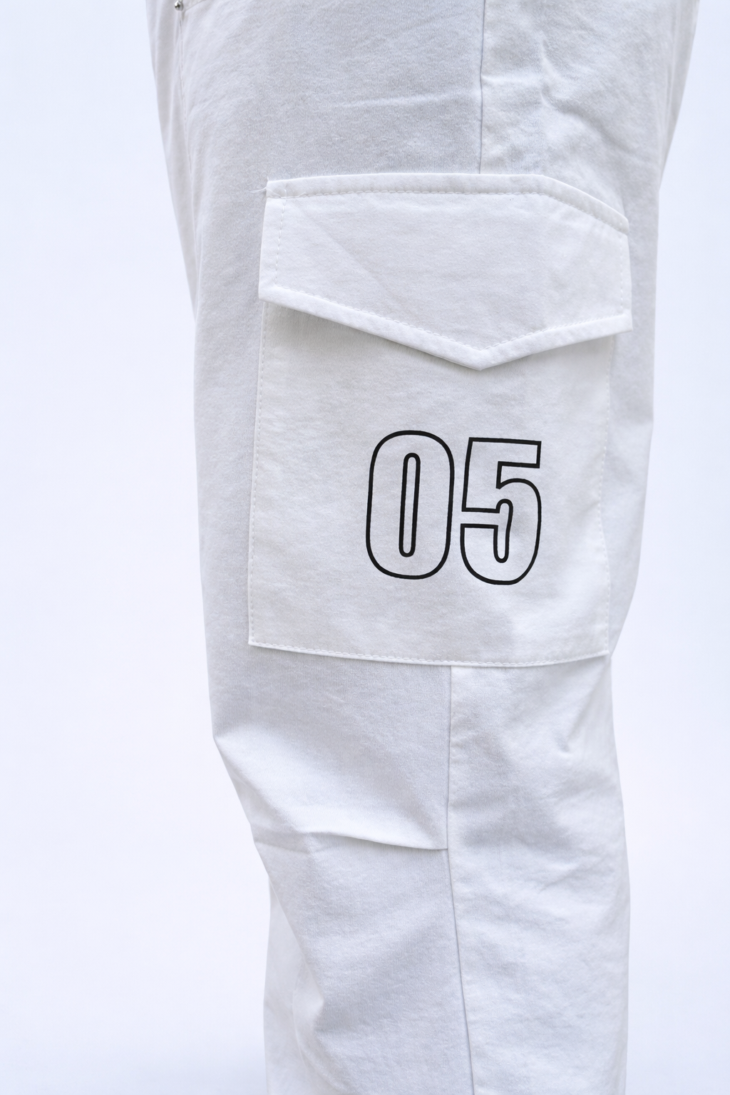 White joggers leg close-up showing flap cargo pocket with bold “05” graphic