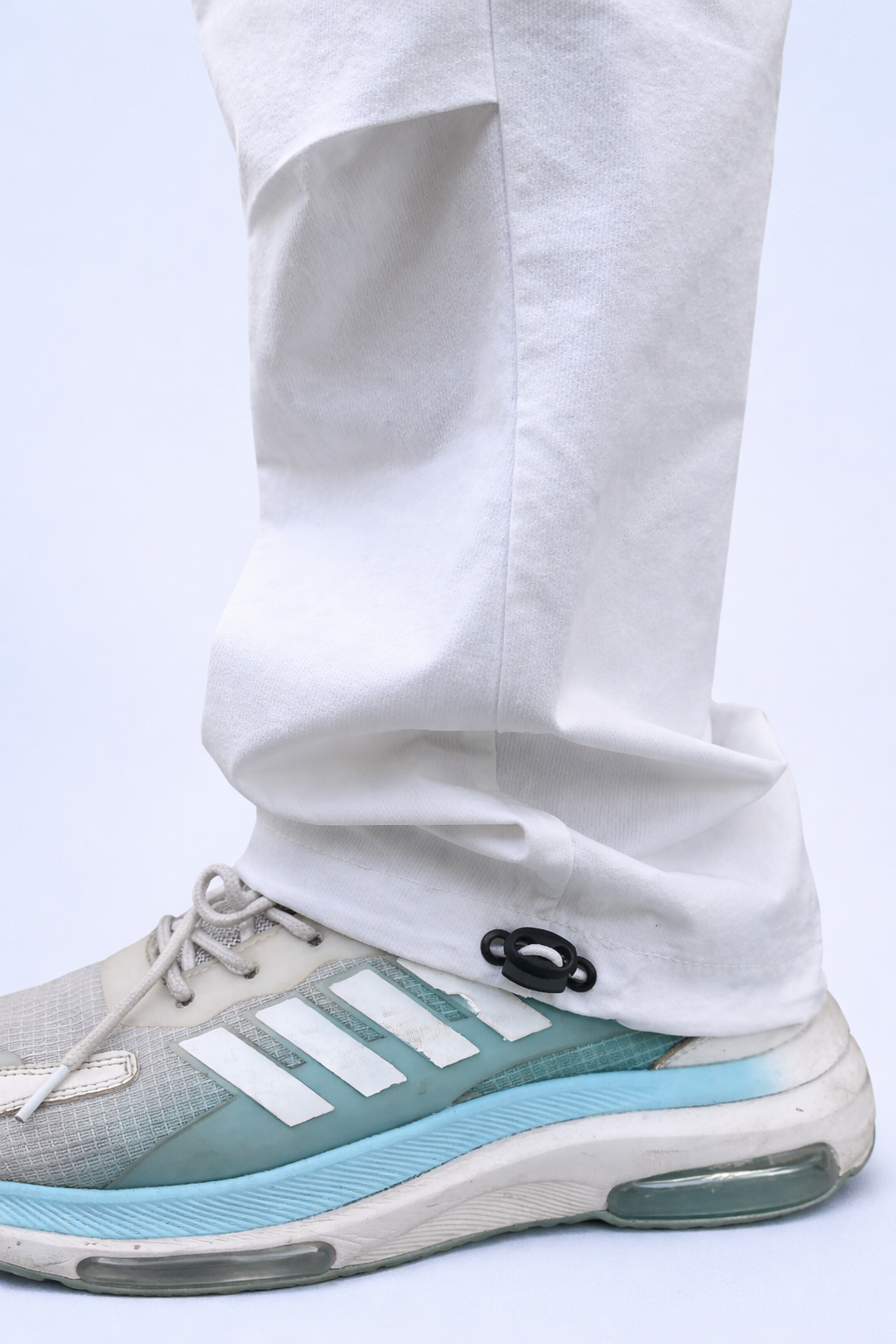 White joggers cuff close-up with drawstring and black ring detail near sneakers