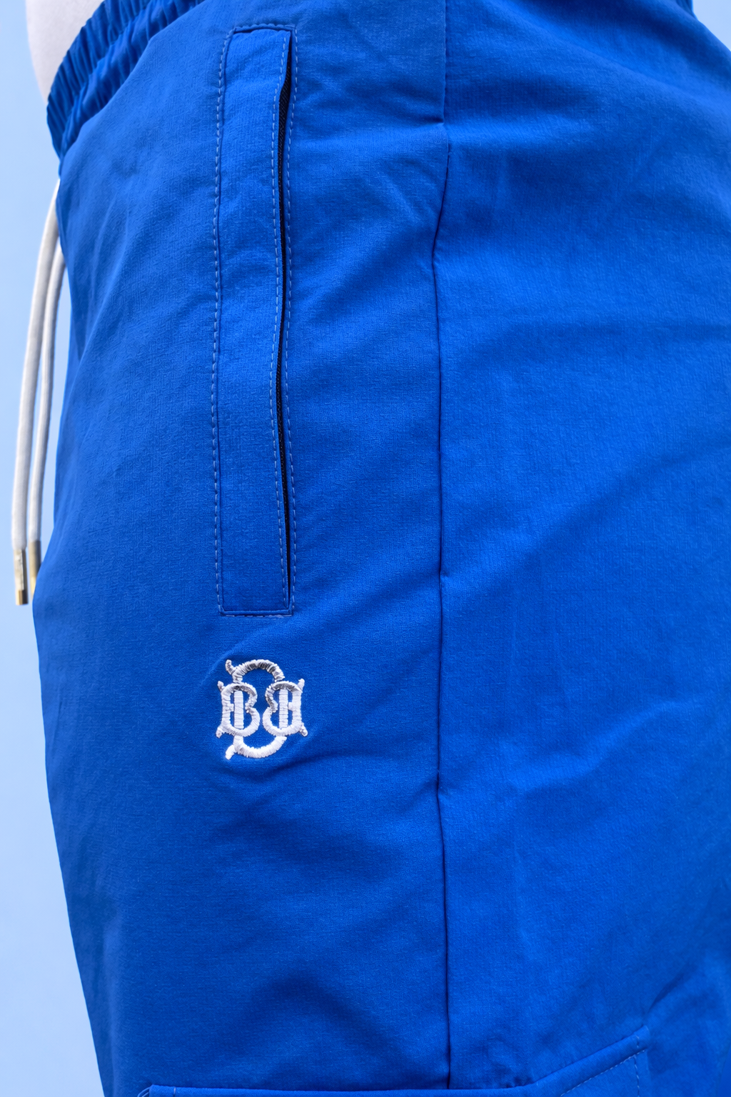 Blue cargo jogger pants close-up of front pocket seam and small embroidered logo