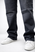 Close-up of dark denim jeans with relaxed bootcut shape and cuffed hem over sneakers