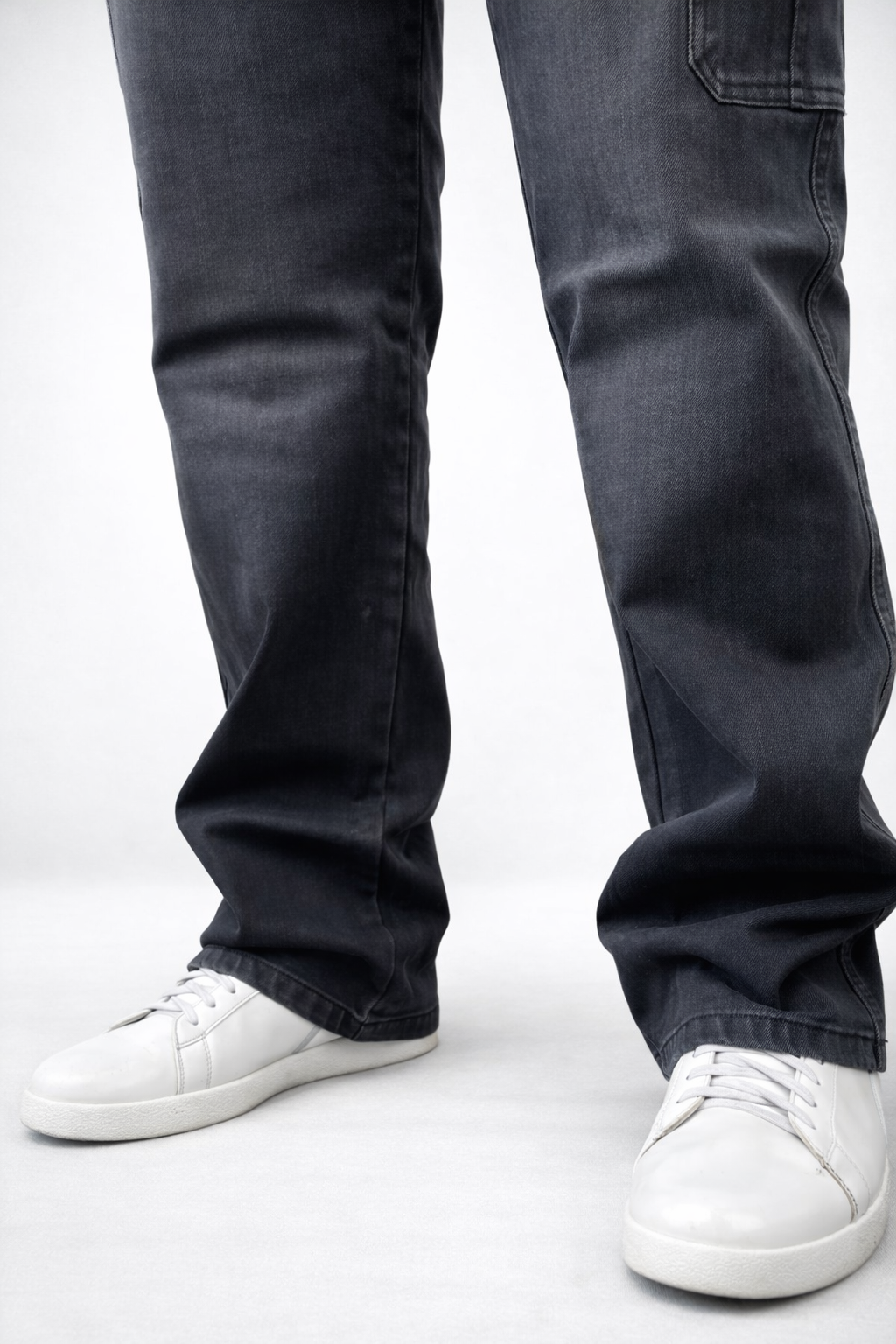 Close-up of dark denim jeans with relaxed bootcut shape and cuffed hem over sneakers