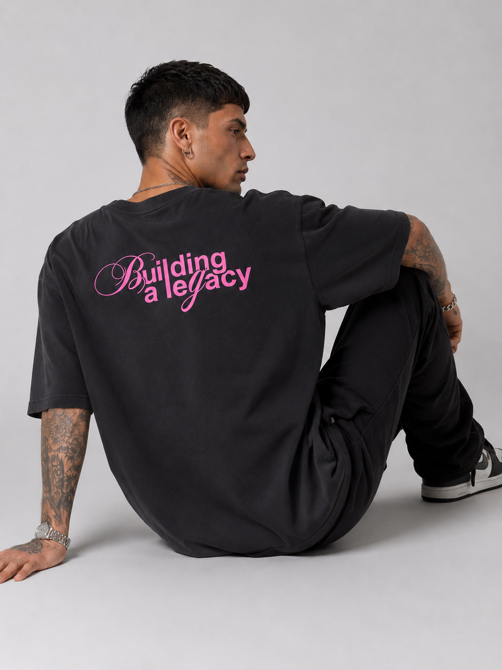 Black drop-shoulder tee with large pink "Building a legacy" script on back