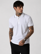 White polo shirt on model, black-trim collar, short sleeves, small chest logo detail.