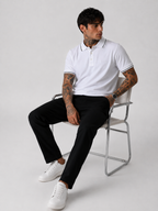 White polo shirt with black collar trim and sleeve cuffs, worn with dark pants.