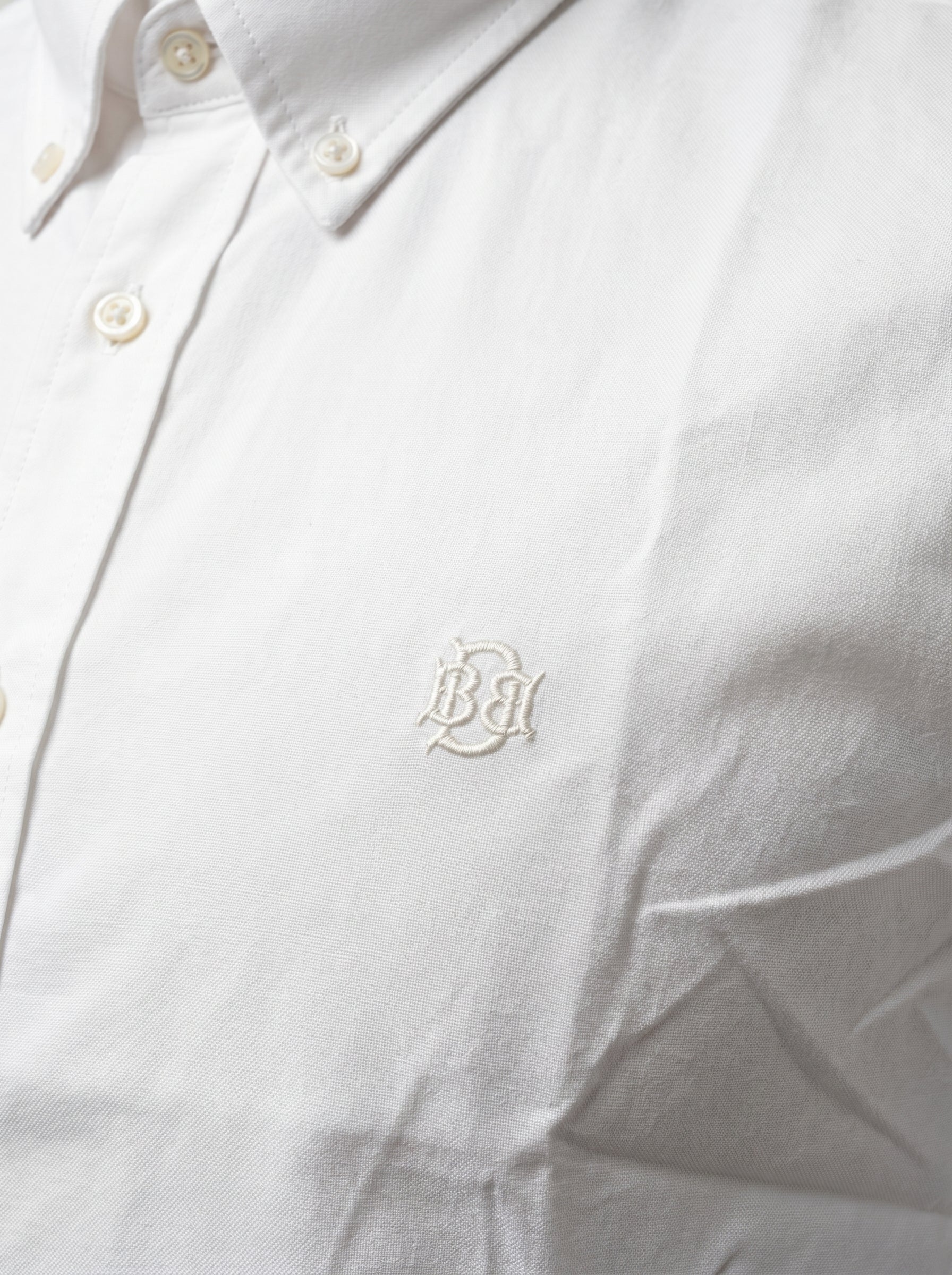White oxford shirt close-up with tonal monogram on textured fabric