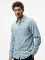 Light blue denim long-sleeve button-up shirt with chest pocket and curved hem