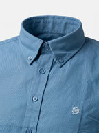 Indigo-blue oxford shirt collar with button placket and small chest monogram.