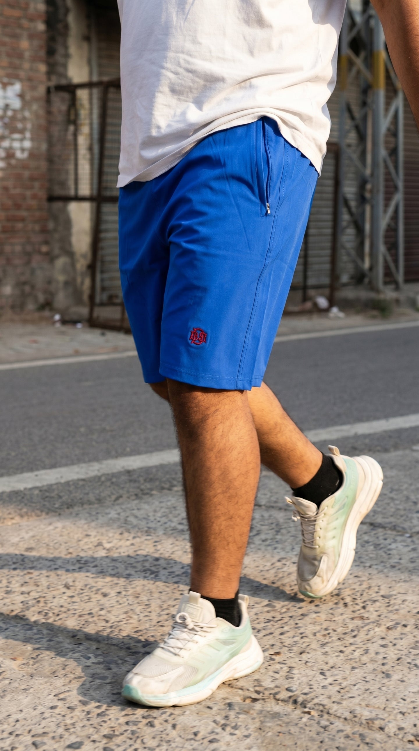 Blue tech shorts with front zip fly, side pockets, red logo on leg