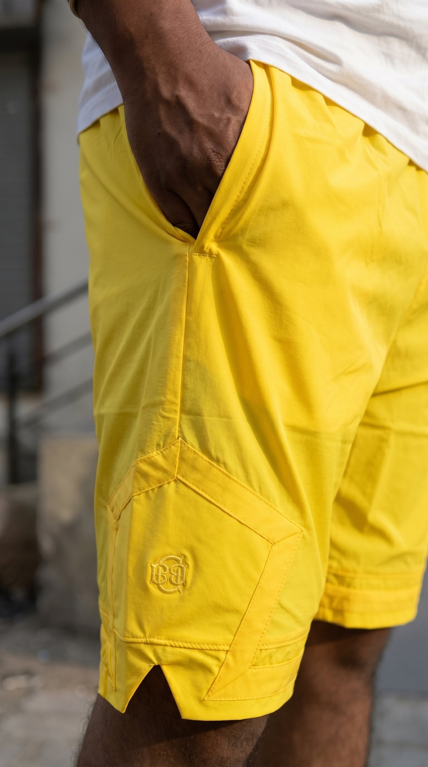 Yellow cargo shorts close-up of pentagonal pocket with small embroidered logo