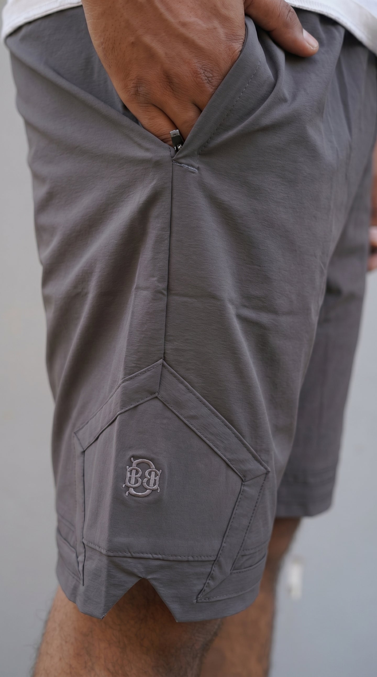 Grey cargo shorts close-up of pentagonal pocket with embroidered logo patch