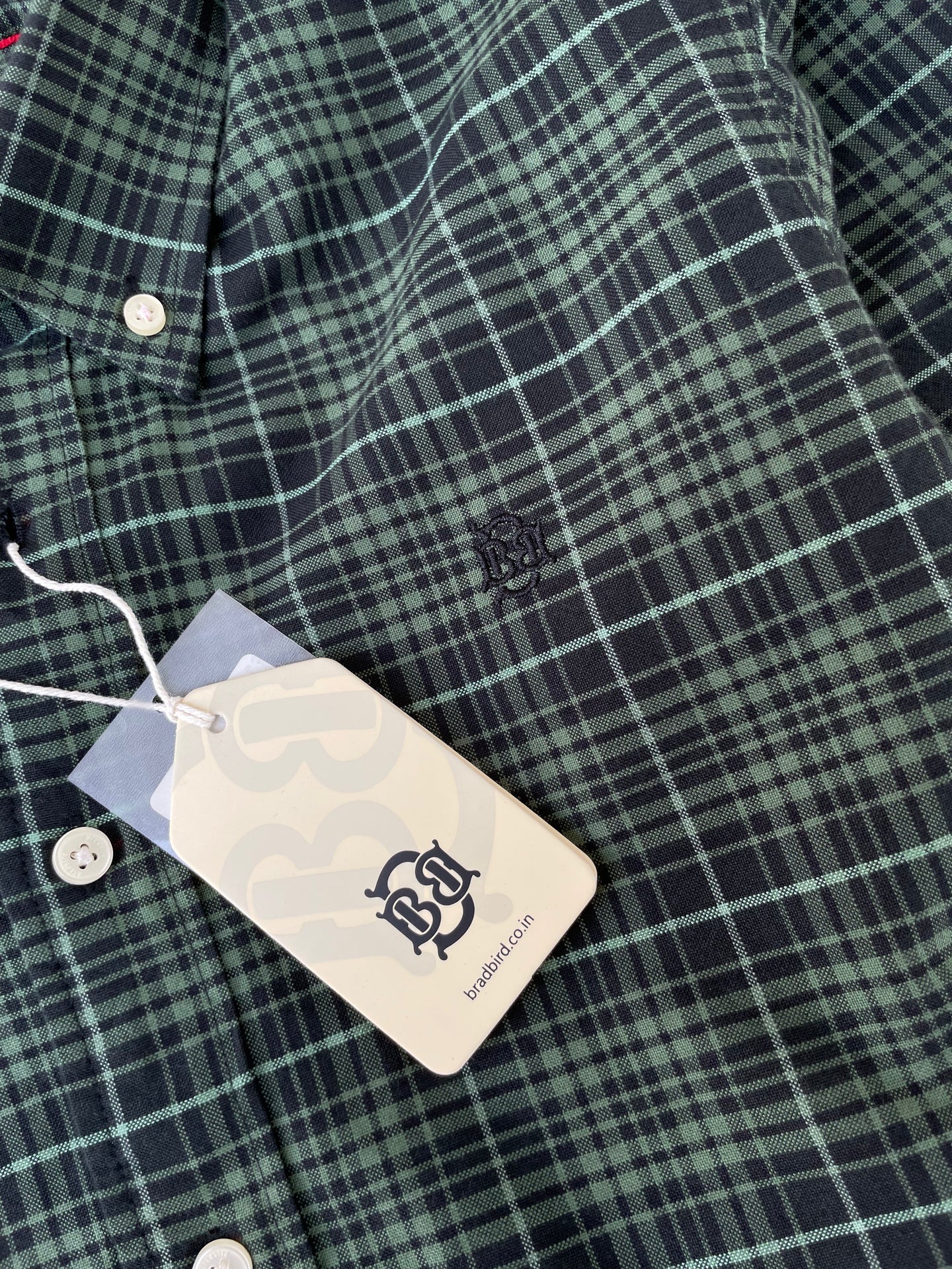 Green check oxford shirt with small chest logo and hang tag near buttons