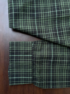 Green plaid oxford shirt cuff and folded hem on dark green fabric