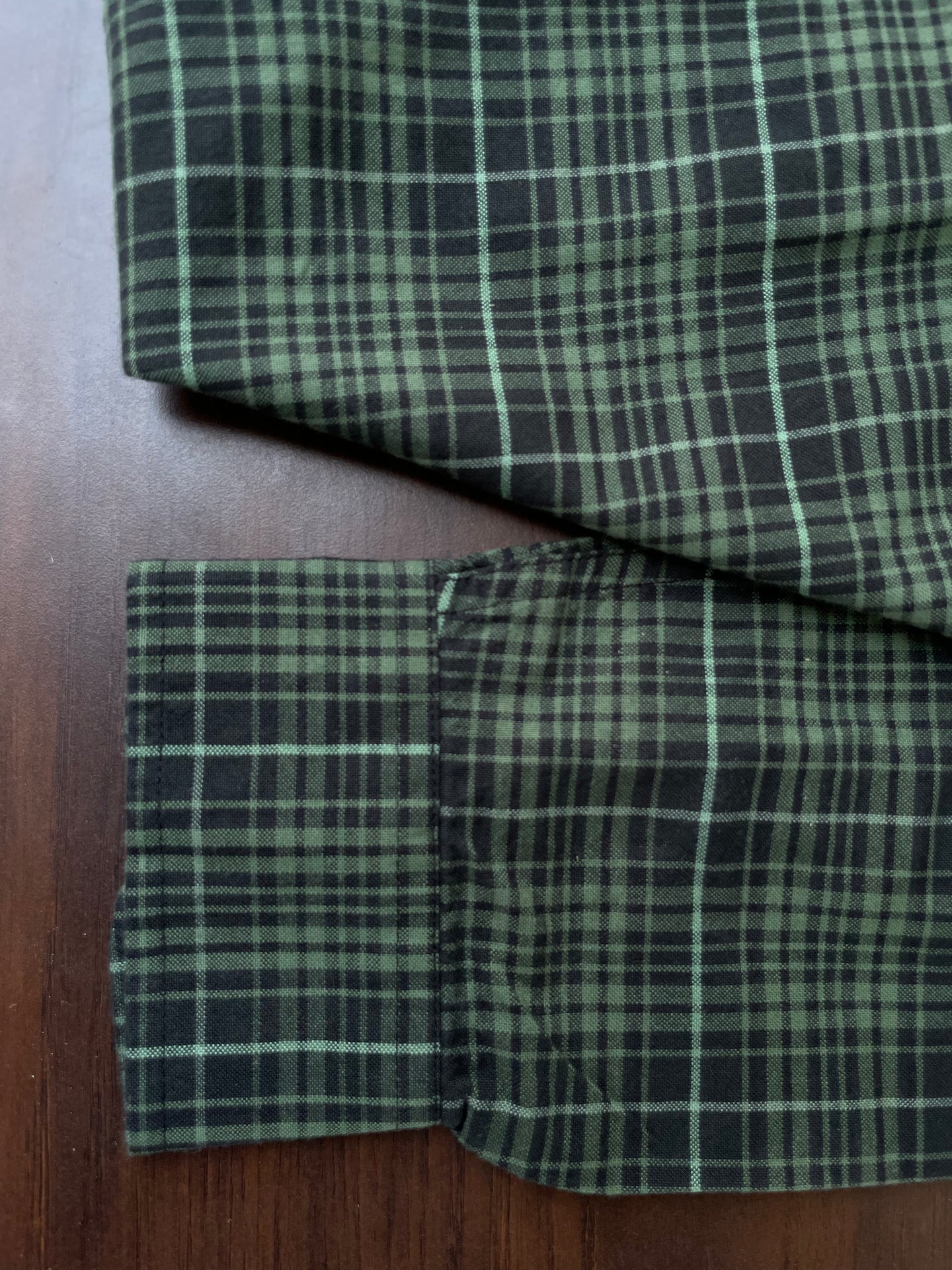 Green plaid oxford shirt cuff and folded hem on dark green fabric