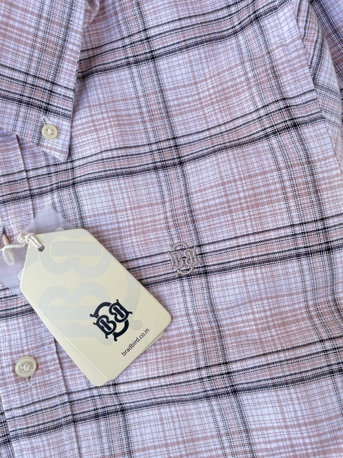 Pink windowpane check oxford shirt fabric close-up with white buttons and hanging tag