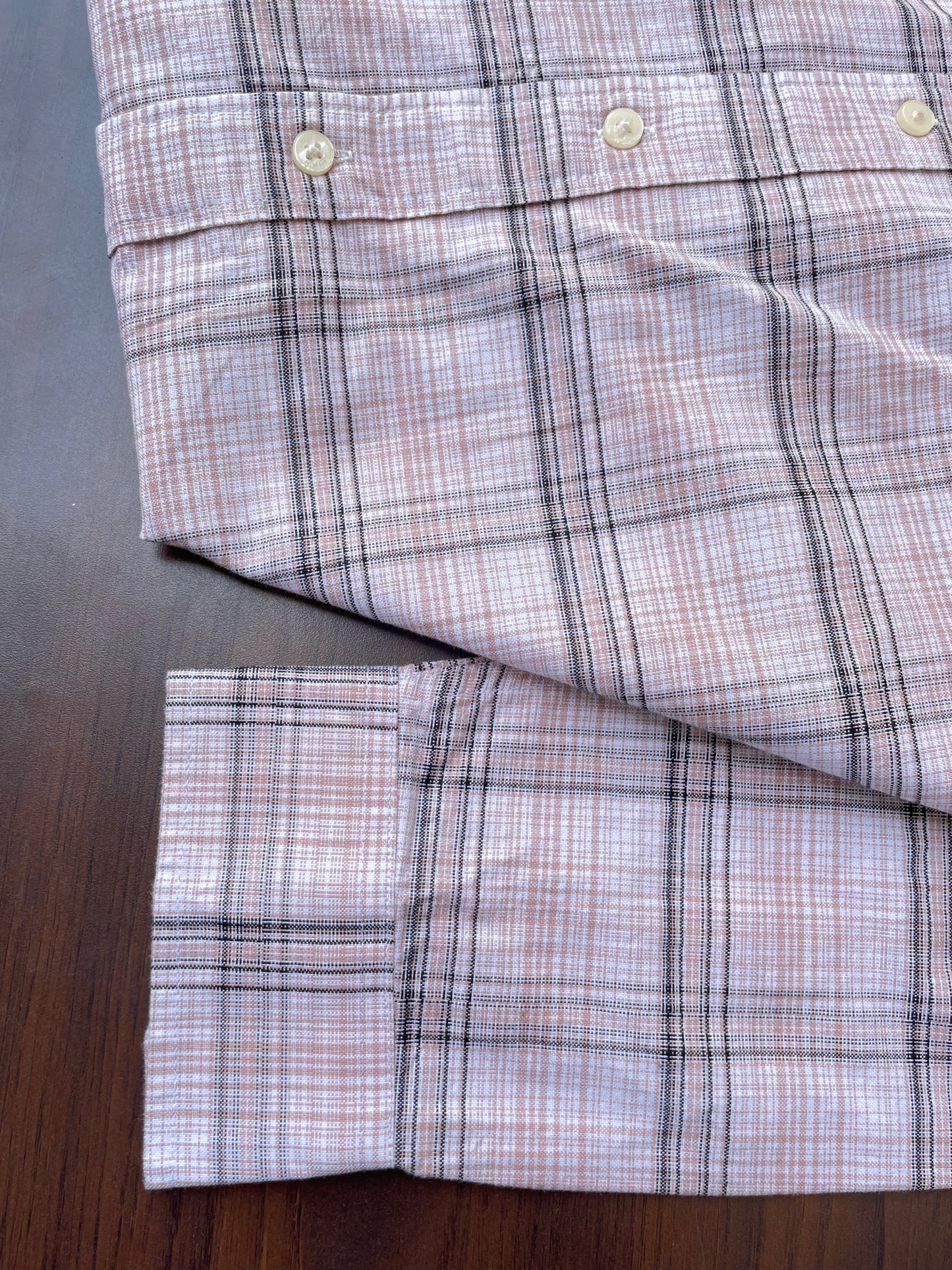 Pink oxford check shirt hem and sleeve cuffs with white buttons, folded