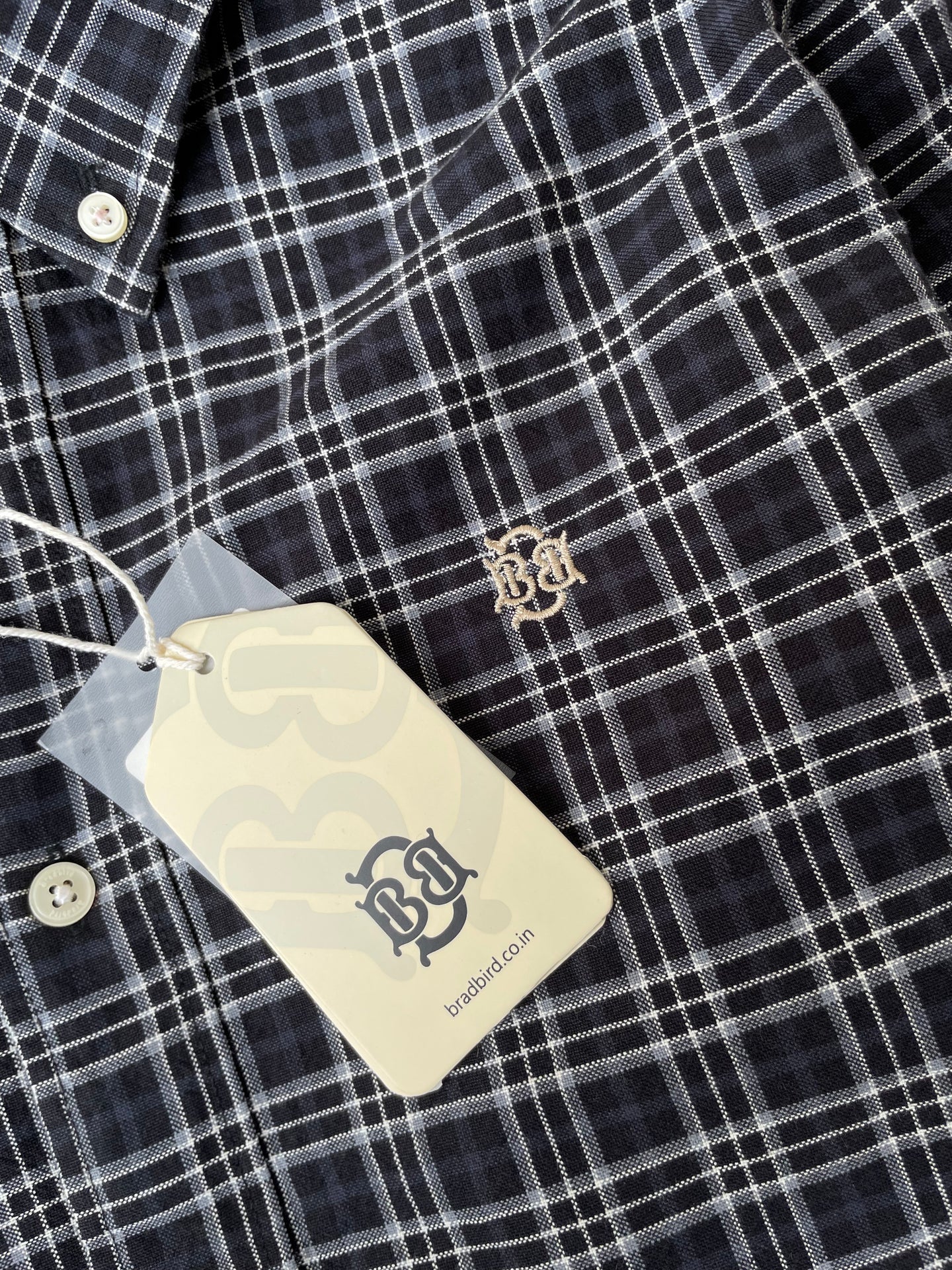 Dark and white check shirt fabric with small gold crest logo on chest