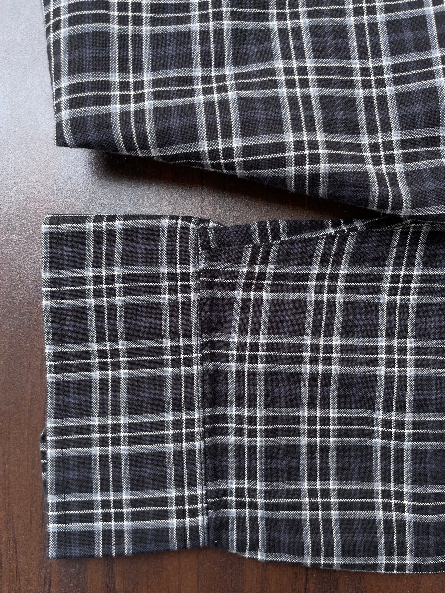 Close view of dark plaid check shirt cuffs and hem on a wooden surface