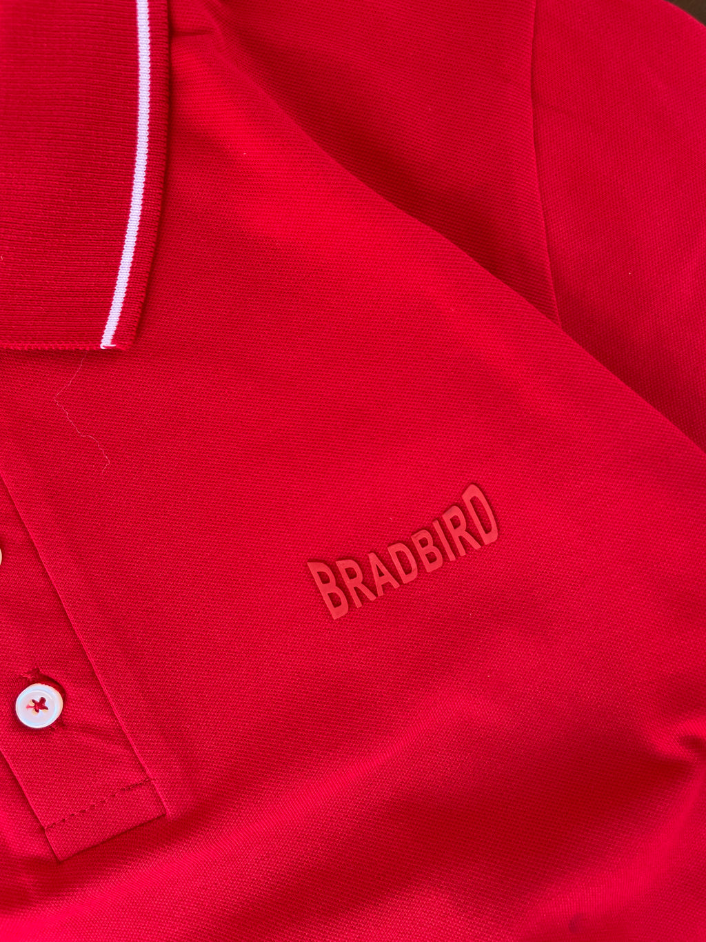 Close-up red polo with white tipping collar and BRADBIRD logo on chest