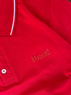 Close-up red polo with white tipping collar and BRADBIRD logo on chest