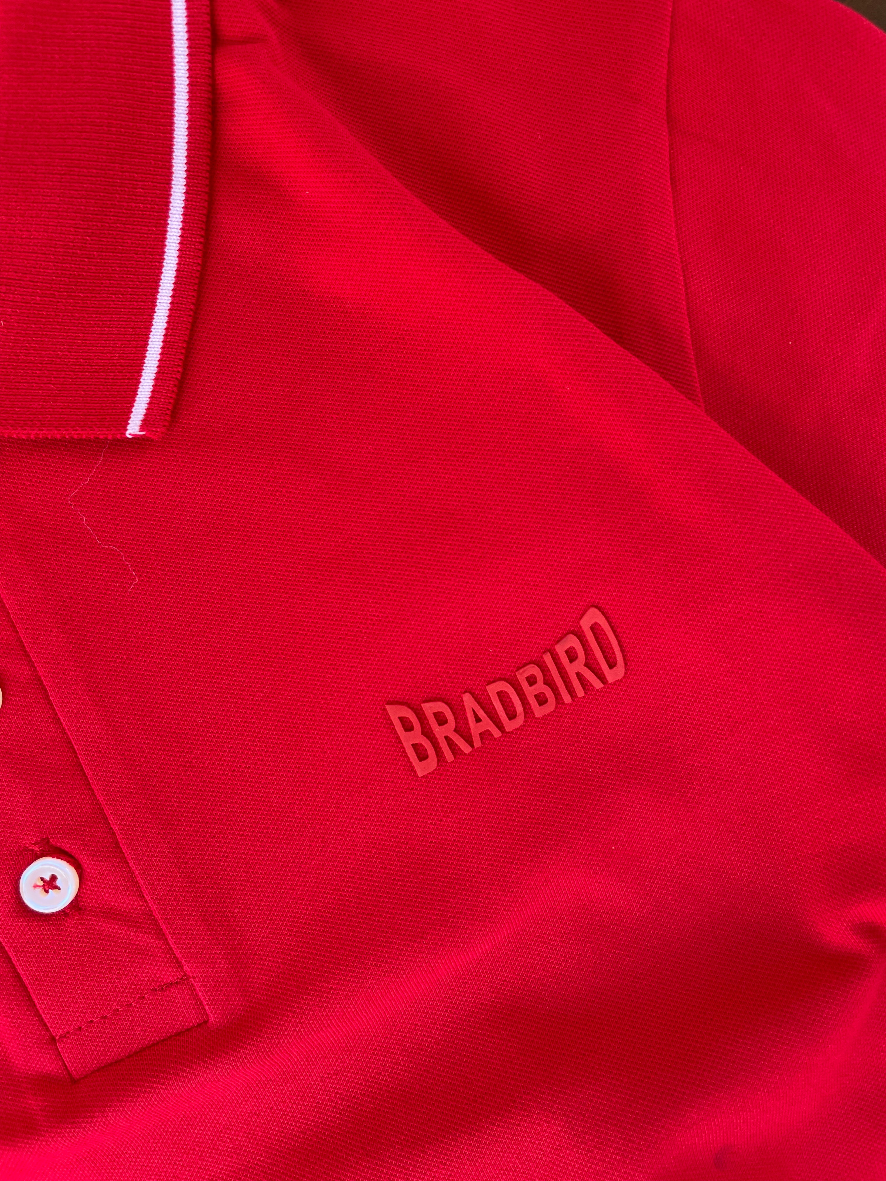 Close-up red polo with white tipping collar and BRADBIRD logo on chest