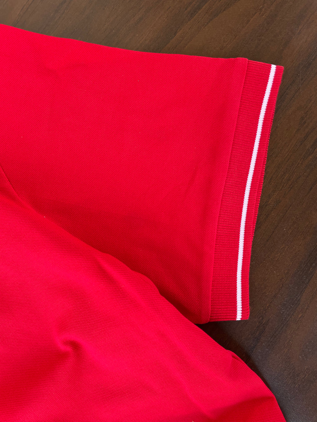 Red polo sleeve and hem with white striped tipping detail along the cuff