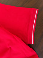 Red polo sleeve and hem with white striped tipping detail along the cuff