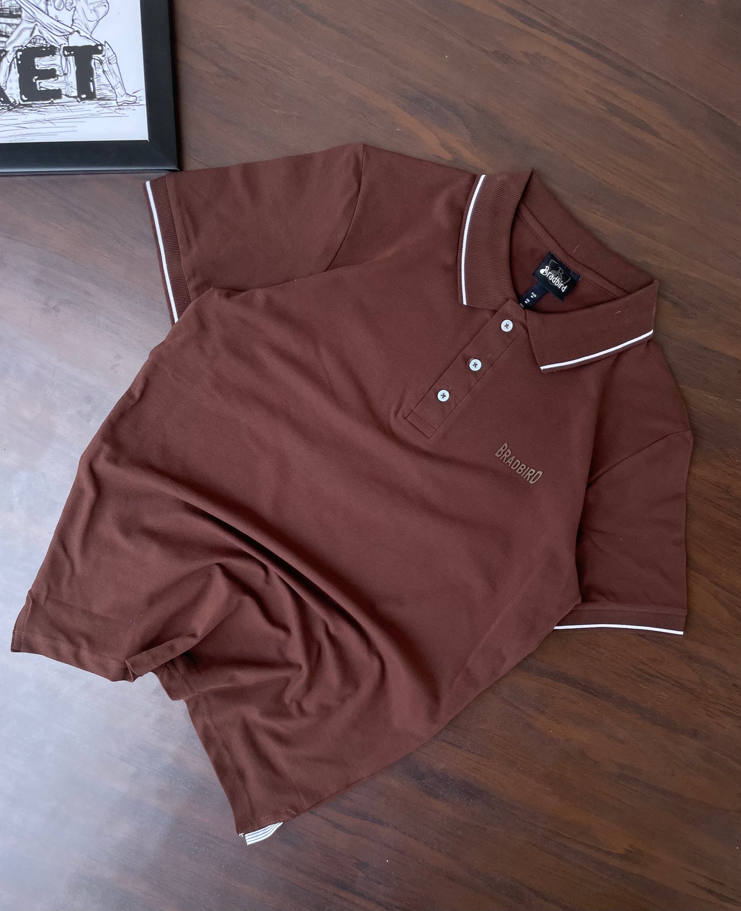 Brown polo shirt folded, white-trim collar and sleeve stripes, 3-button placket