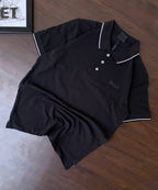 Black polo shirt, folded flat, white-tipped collar and sleeve trim