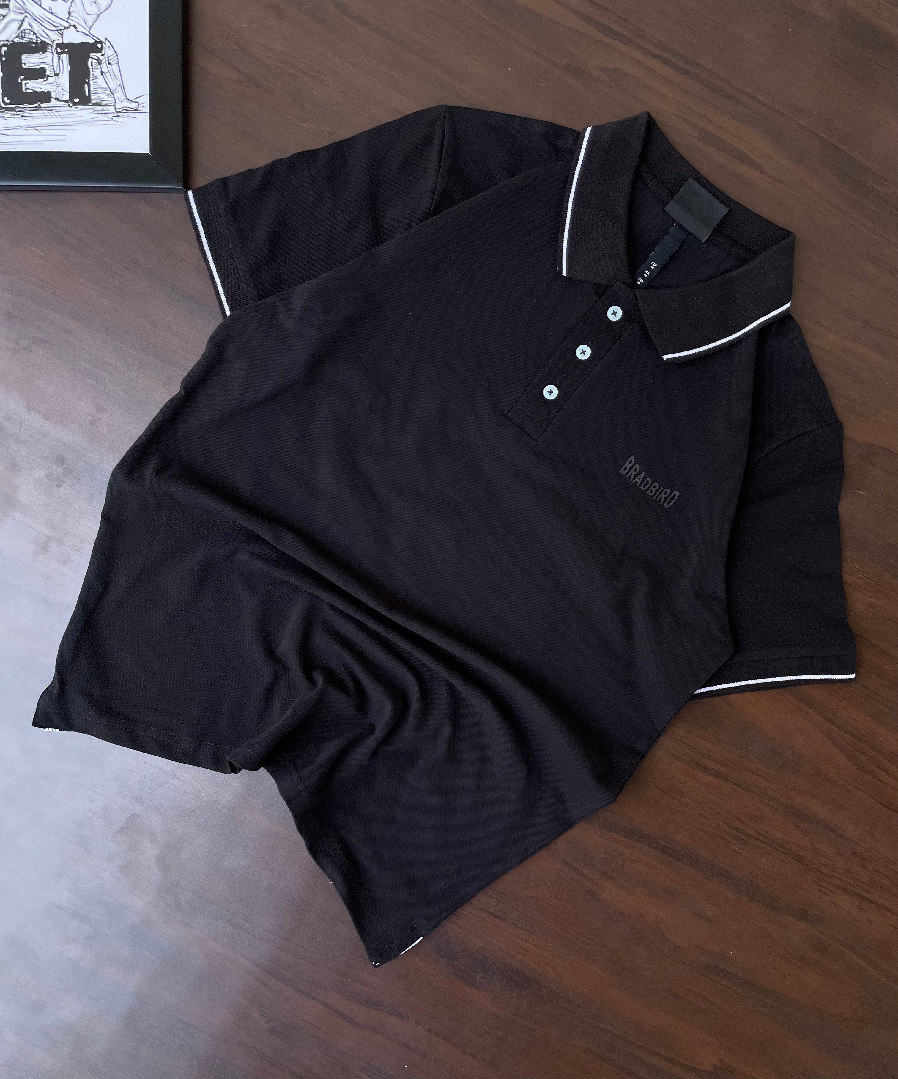 Black polo shirt, folded flat, white-tipped collar and sleeve trim