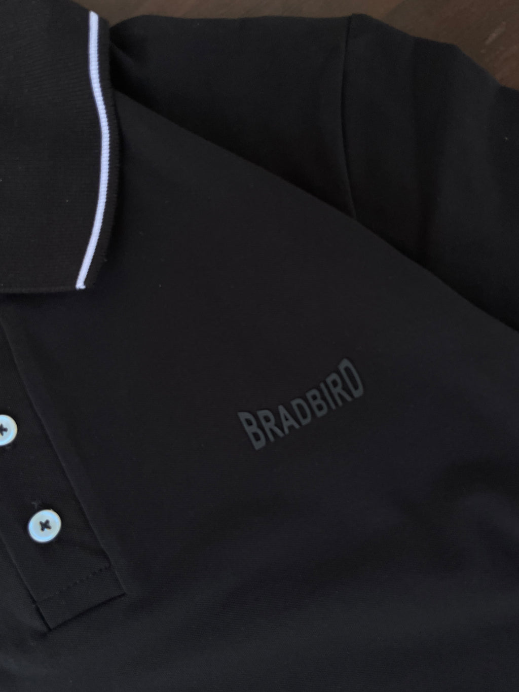 Black polo shirt close-up: white collar edge, button placket, embroidered logo