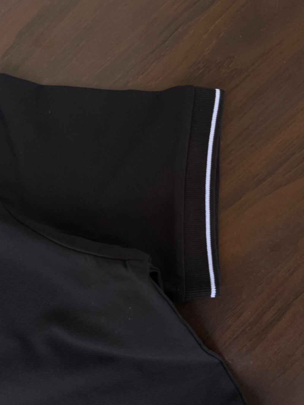 Black polo shirt sleeve trim with white stripe band at cuff