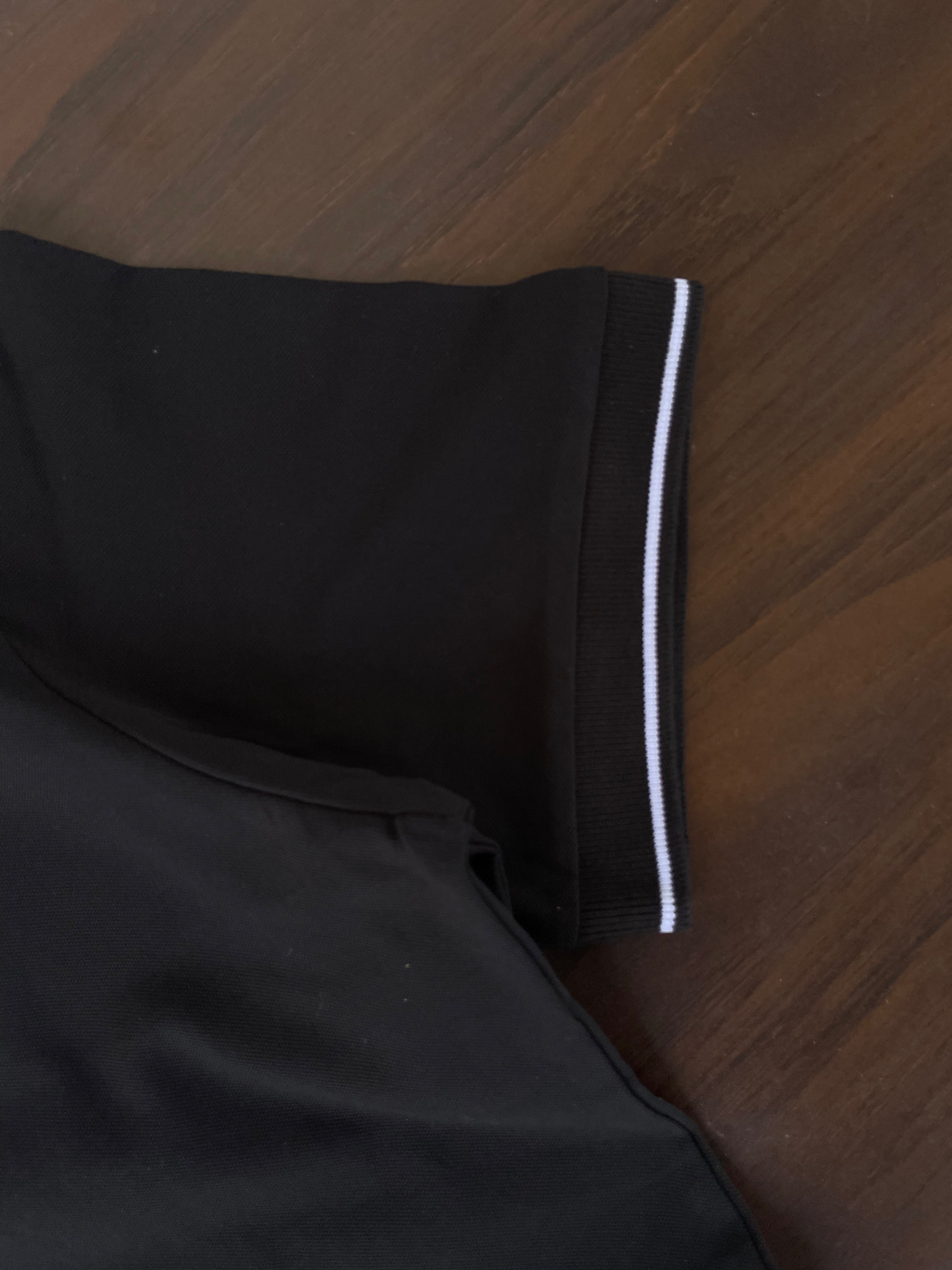 Black polo shirt sleeve trim with white stripe band at cuff