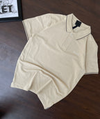 Cream polo shirt laid flat with navy-trim collar, button placket, Bradbird chest logo.