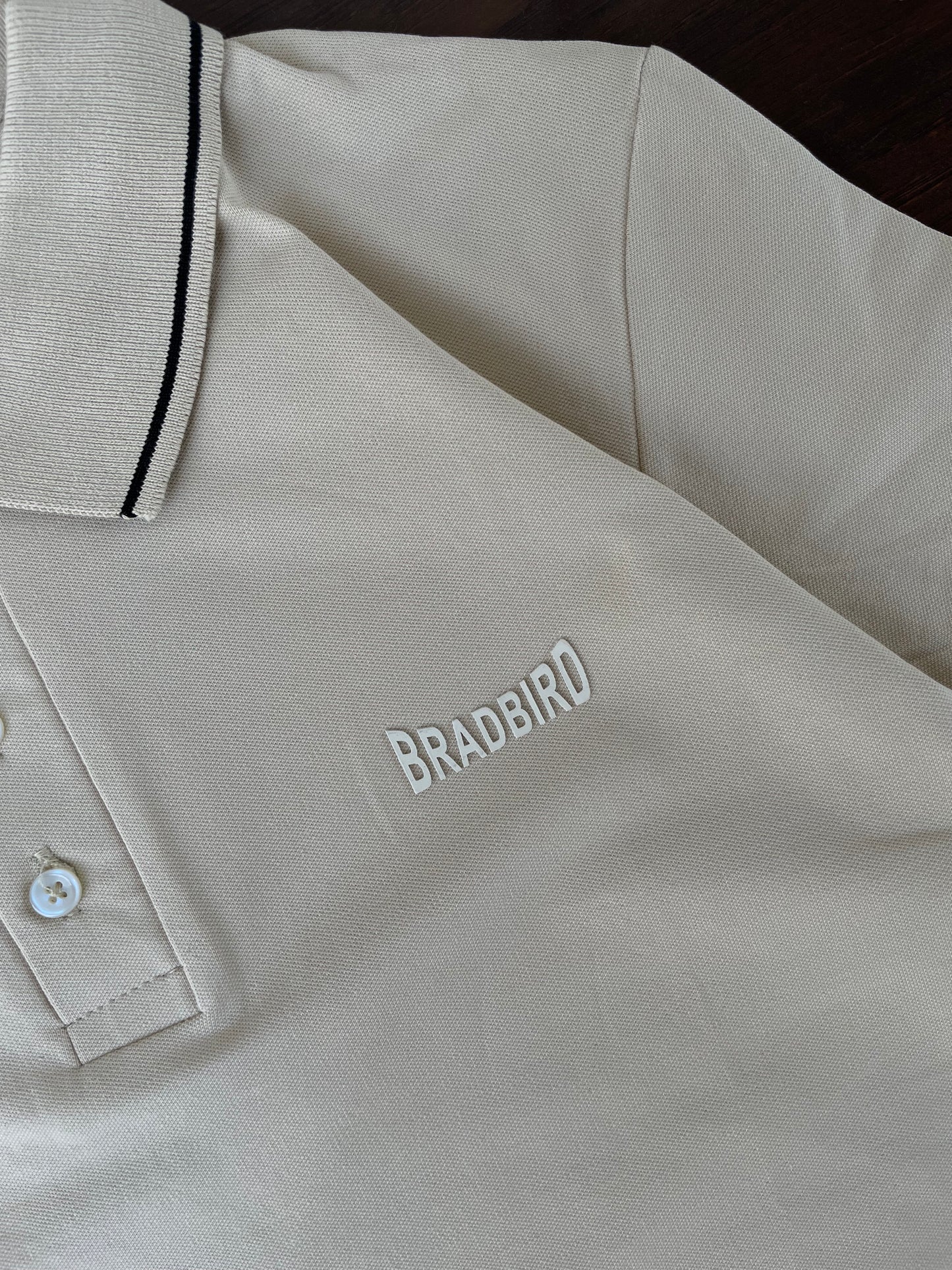 Cream polo close-up: button placket, logo embroidery, and navy collar trim