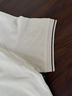 Cream polo shirt sleeve with navy-trim cuff and side hem detail.