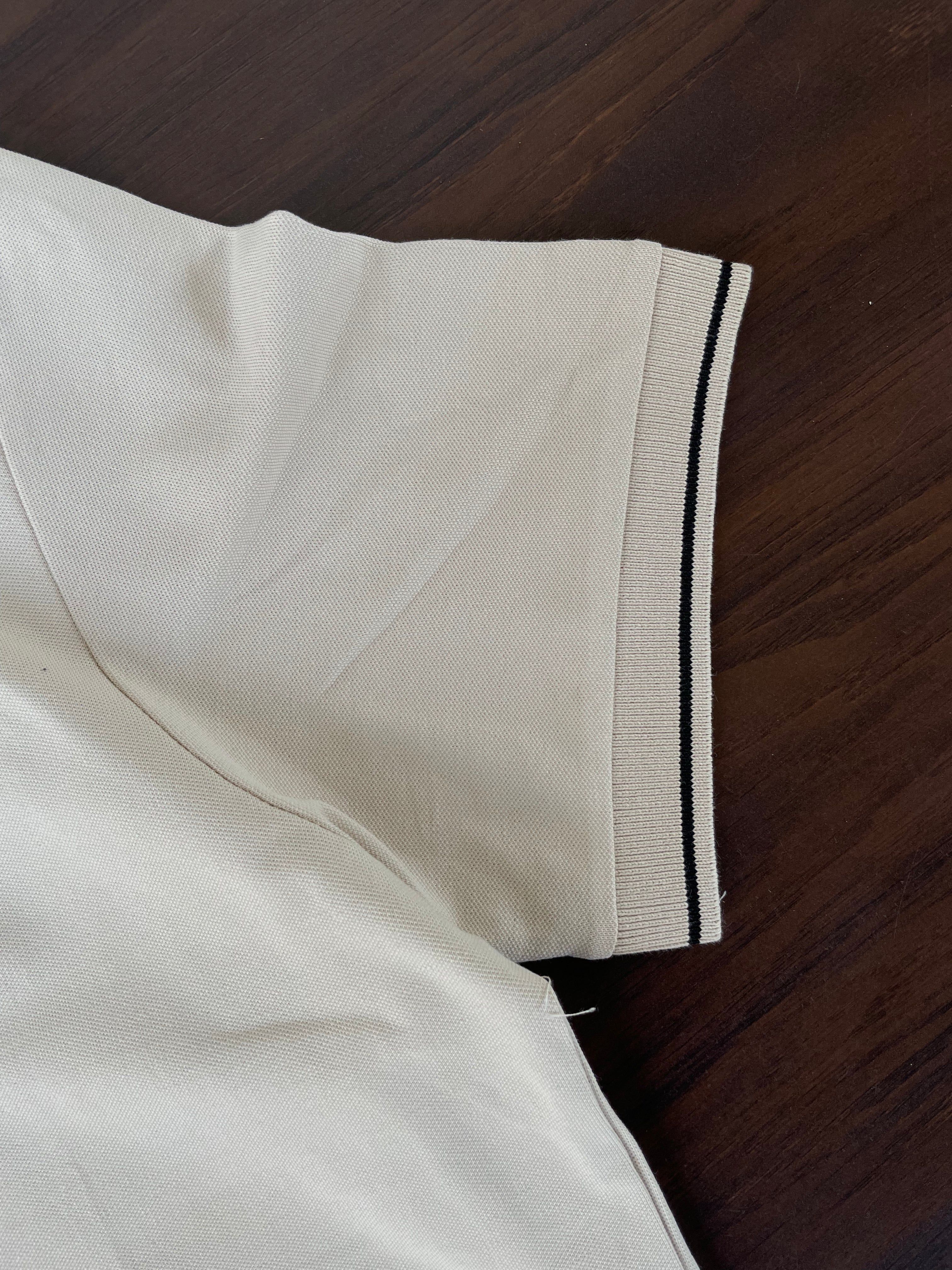 Cream polo shirt sleeve with navy-trim cuff and side hem detail.